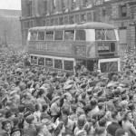 A number 3 double-decker bus slowly pushes its way through the huge crowds gathered in Whitehall to hear Churchill’s Victory speech and celebrate Victory in Europe Day
