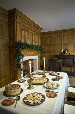 A view of the 1630 period room at Christmas Past. The photograph sows the table laid for a feast of sweetmeats and the mantel above the fireplace decorated with evergreens.
